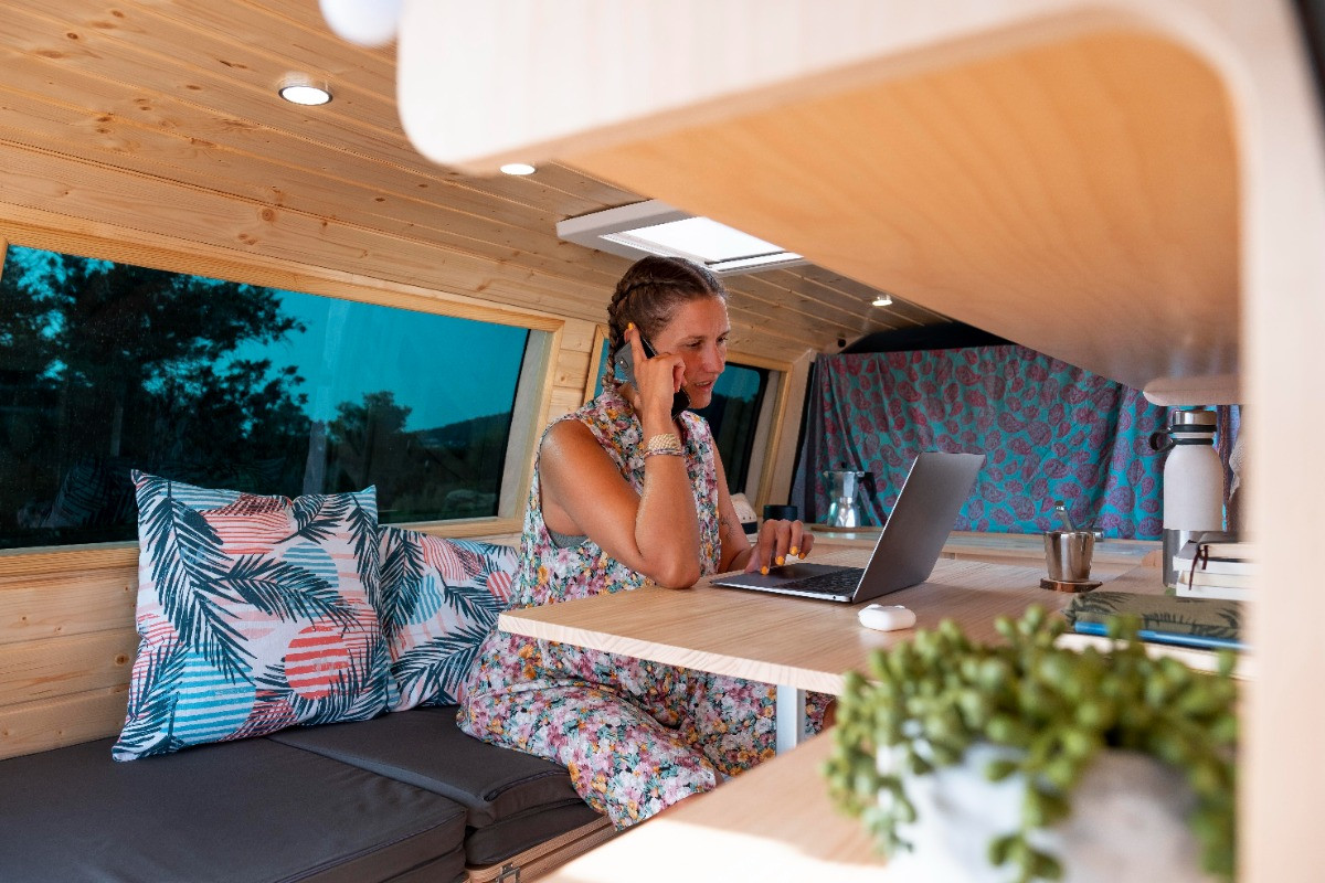 woman on phone while working on laptop in rv